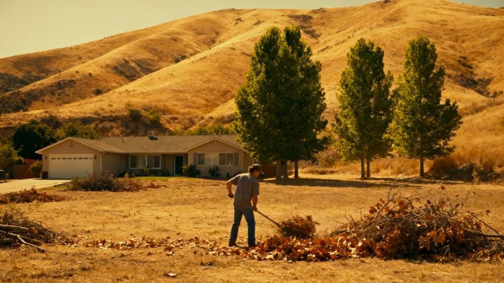 Homeowner clearing brush around a house for wildfire season.